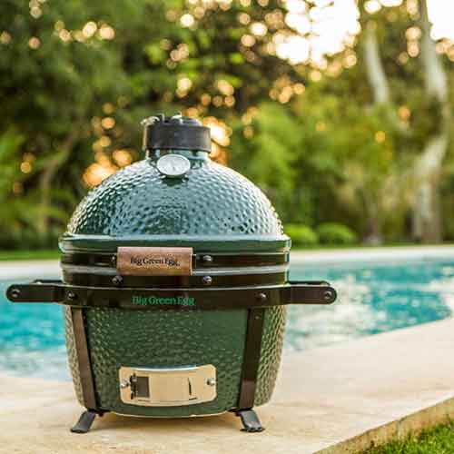 Minimax size big green egg sitting on the stone next to a pool.